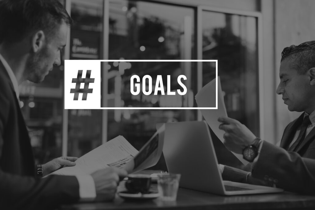 two men are sitting and reading something, and hashtag is given goals