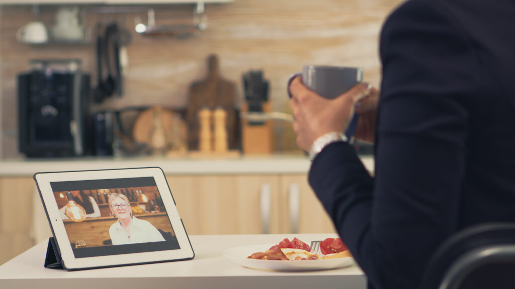 Business woman on a video call with her mother during breakfast. Using modern online internet web technology to chat via webcam videoconference app with relatives, family, friends and coworkers